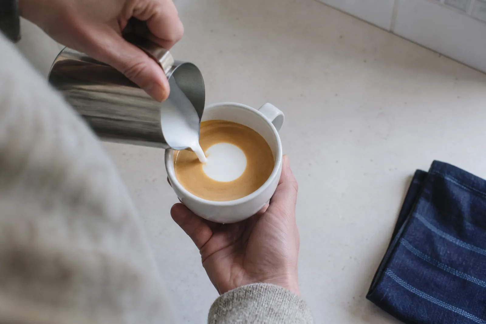 A beginner home barista pouring a simple white circle into a tilted cup of espresso