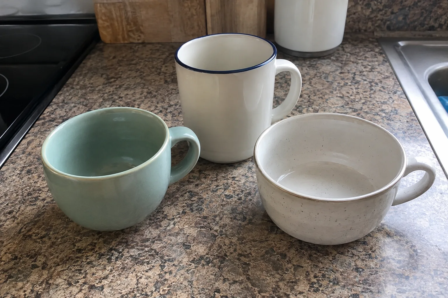 A rounded coffee cup, a tall straight-sided mug and a wide shallow cup on a kitchen counter