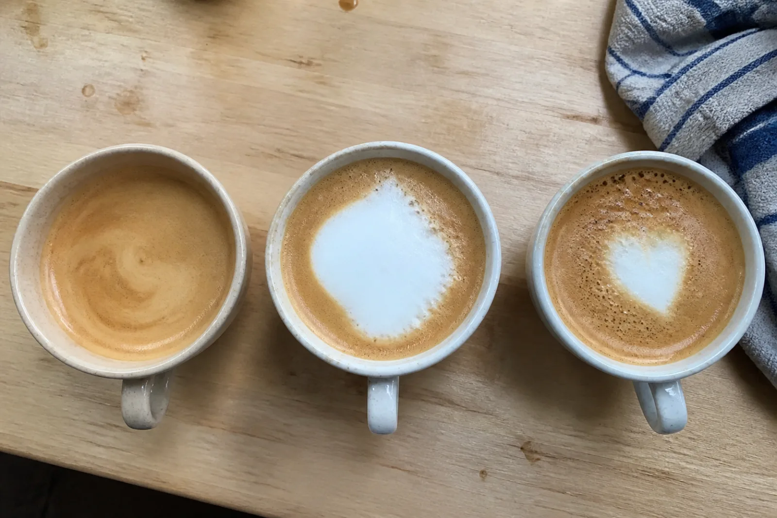 Three home latte art attempts showing no white design, a foam blob, and a small bubbly heart