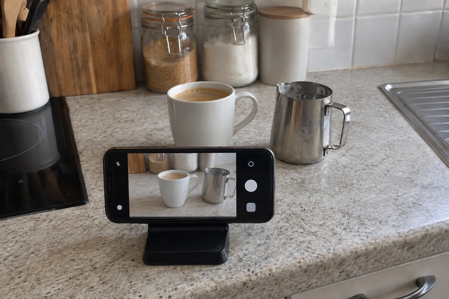 A phone on a tabletop stand with its camera aimed at a cup and milk pitcher