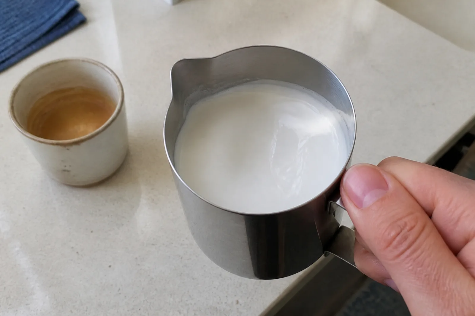 Glossy microfoam swirling smoothly inside a stainless steel milk pitcher on a home kitchen counter