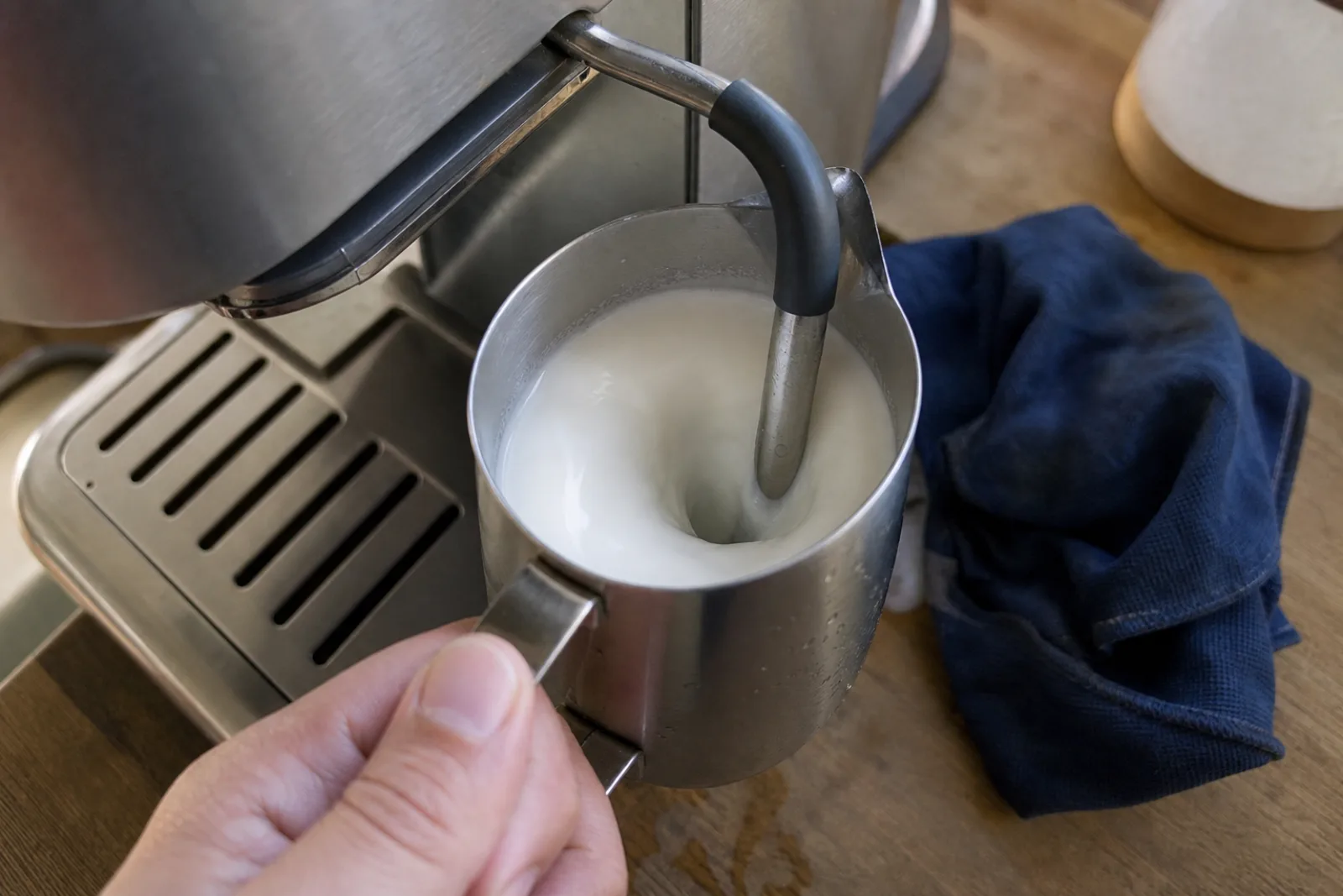 Milk spinning in a small stainless pitcher under a home espresso machine steam wand