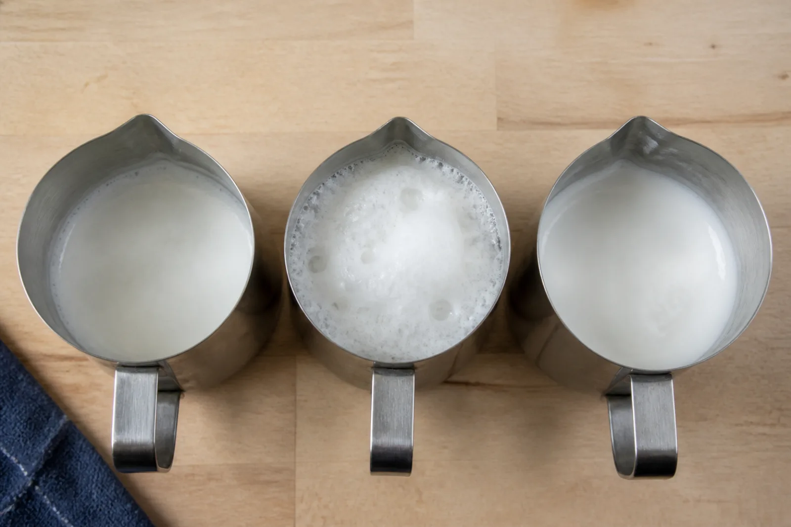 Three pitchers showing thin milk, a dry bubbly foam cap, and glossy pourable microfoam