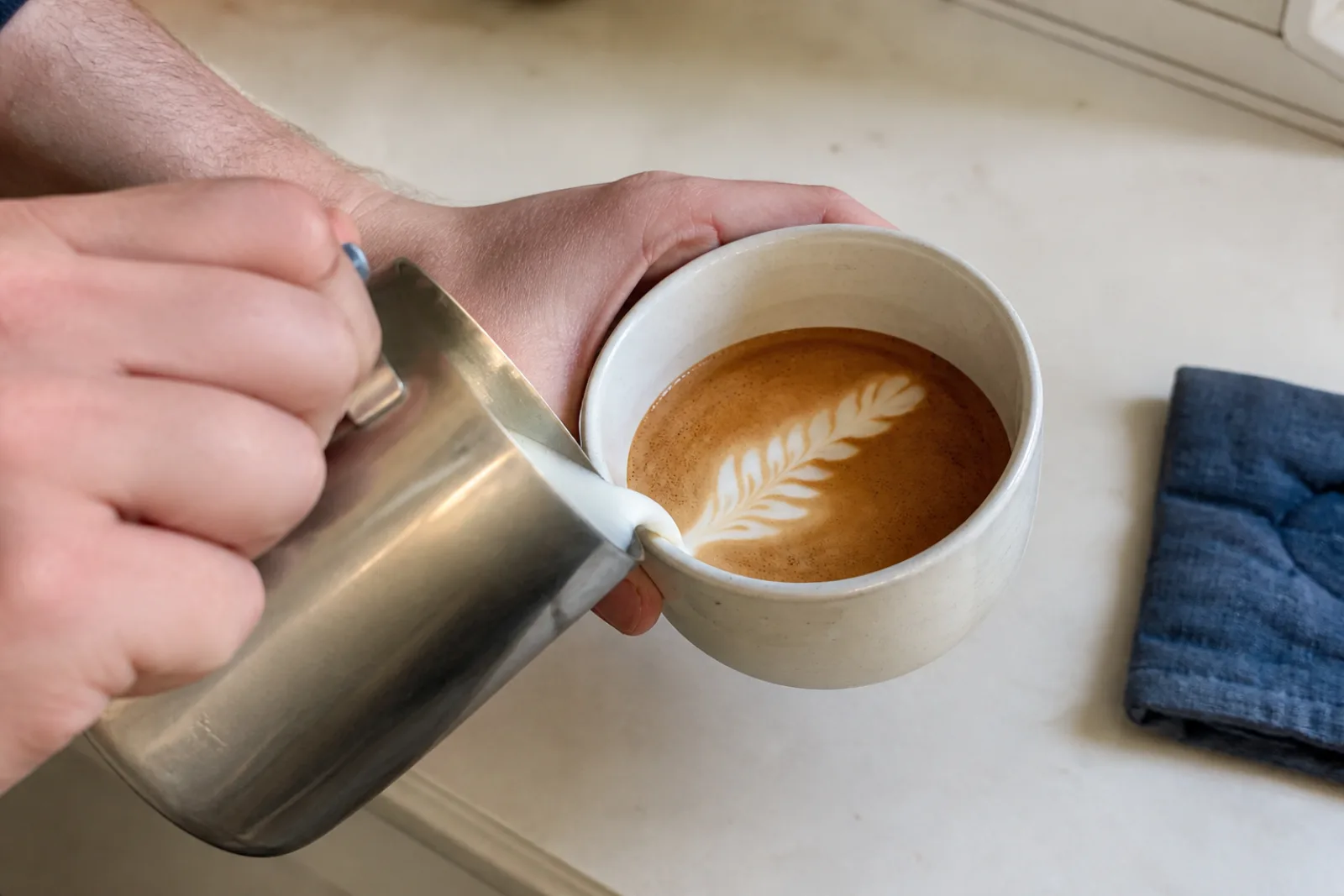 A home barista pouring a narrow rosetta with slightly uneven white leaves